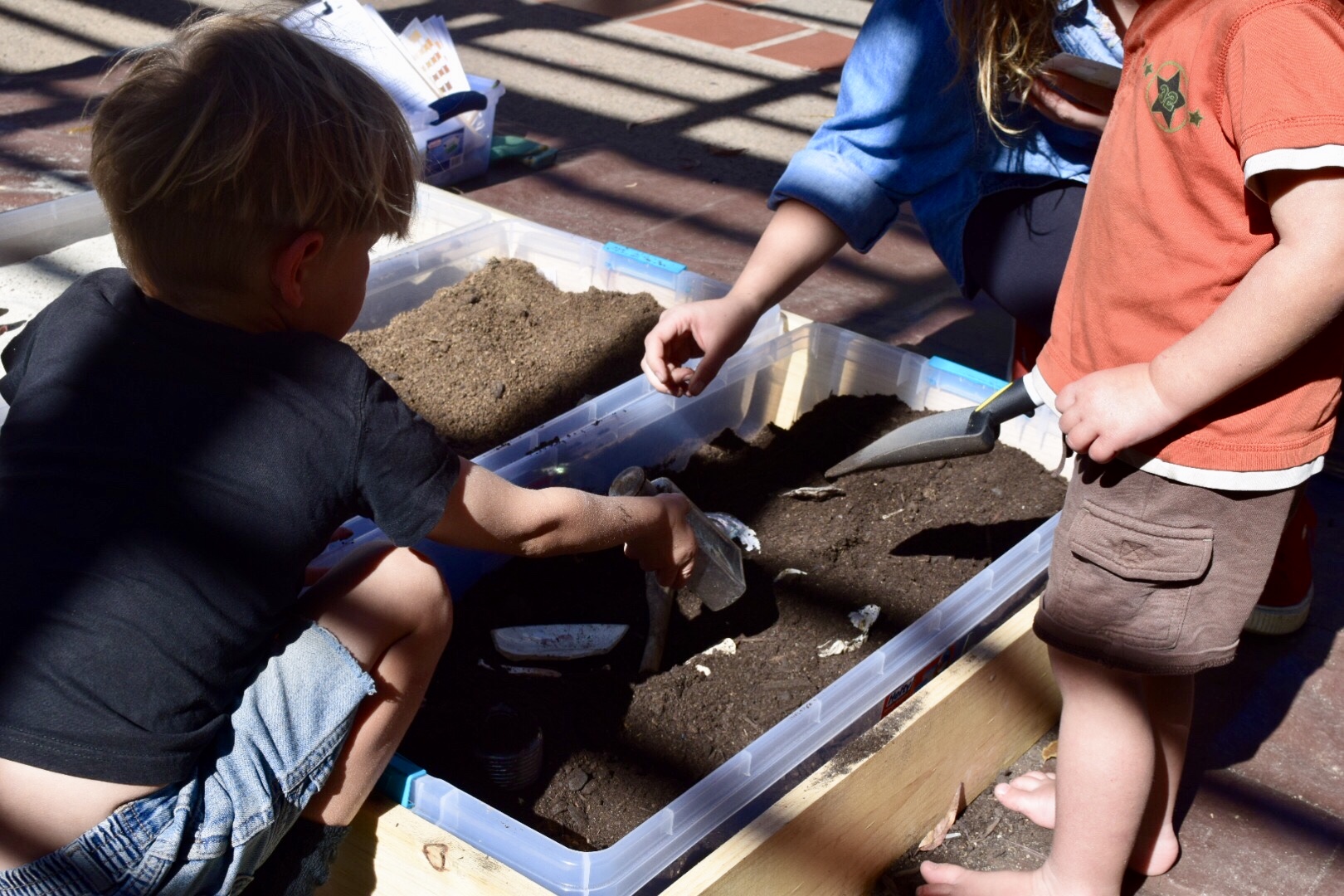 Photo of 2 small children digging with trowels in a large tub of soil to uncover artifacts and simulate excavation